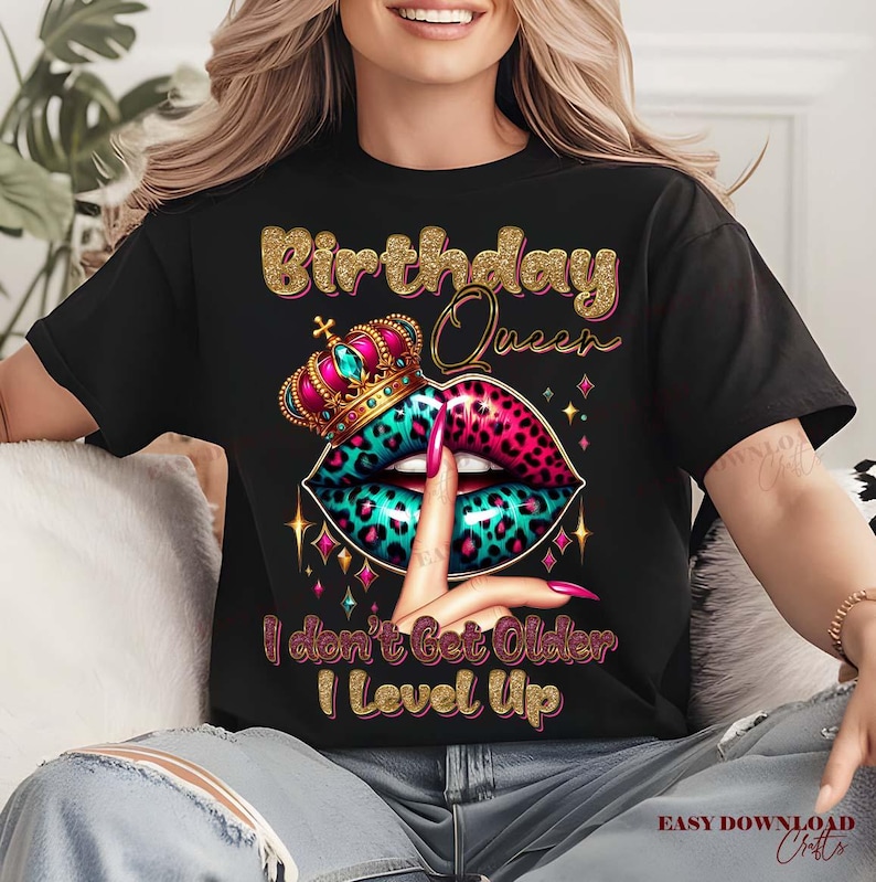 May include: Black t-shirt with a gold glitter design that reads "Birthday Queen." The graphic features a crown, lips with a leopard print design in pink and teal, and a finger to the lips. The text "I don't Get Older I Level Up" is below the lips.