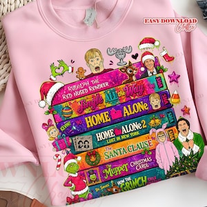 Puede incluir: Una sudadera rosa claro con un estampado gr&aacute;fico de cintas VHS apiladas con t&iacute;tulos de pel&iacute;culas navide&ntilde;as como Home Alone, The Santa Clause y The Muppet Christmas Carol, rodeadas de personajes festivos e iconos navide&ntilde;os.