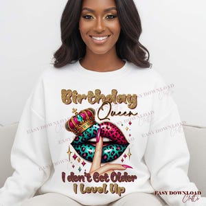 May include: White sweatshirt with a graphic design featuring the text "Birthday Queen". The design includes a crown, lips with a leopard print, and the phrase "I don't Get Older I Level Up".