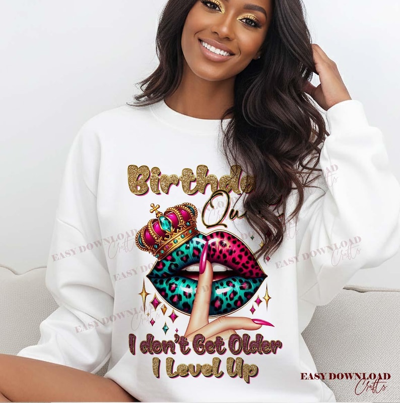 May include: White sweatshirt with a graphic design featuring the text "Birthday Queen" in gold glitter lettering. The design includes a crown, lips with a teal and pink leopard print, and the text "I don't Get Older I Level Up."
