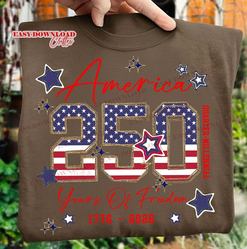 May include: A brown t-shirt with the text "America 250 Years Of Freedom 1776-2026" in red and gold. The number "250" is filled with a stars and stripes pattern, and there are star graphics.