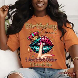 May include: Orange t-shirt with a graphic design featuring the text "Birthday Queen" in gold glitter. The design includes a crown, lips with a leopard print, and the text "I don't Get Older I Level Up."