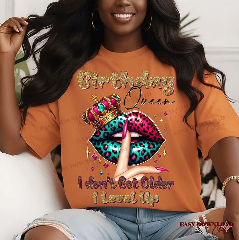 May include: Orange t-shirt with a graphic design featuring the text "Birthday Queen" in gold glitter. The design includes a crown, lips with a leopard print, and the text "I don't Get Older I Level Up."