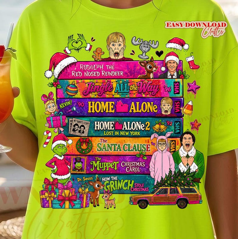 Puede incluir: Una camiseta de color verde lima ne&oacute;n con un estampado gr&aacute;fico de cintas VHS apiladas etiquetadas con t&iacute;tulos de pel&iacute;culas navide&ntilde;as como Home Alone, The Santa Clause y The Muppet Christmas Carol, rodeadas de personajes festivos.