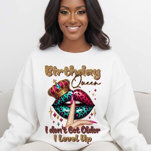 May include: White sweatshirt with a graphic design featuring the text "Birthday Queen" in gold glitter lettering. The design includes a crown, lips with a leopard print, and the text "I don't Get Older I Level Up."
