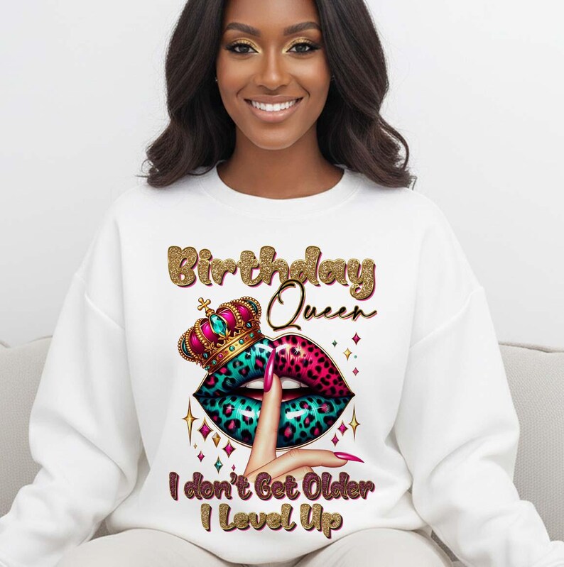 May include: White sweatshirt with a graphic design featuring the text "Birthday Queen" in gold glitter lettering. The design includes a crown, lips with a leopard print, and the text "I don't Get Older I Level Up."