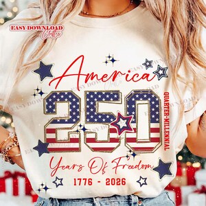 May include: Cream-colored t-shirt with the text "America 250 Years Of Freedom 1776-2026". The number 250 is filled with a blue star pattern and red stripes, surrounded by blue stars.