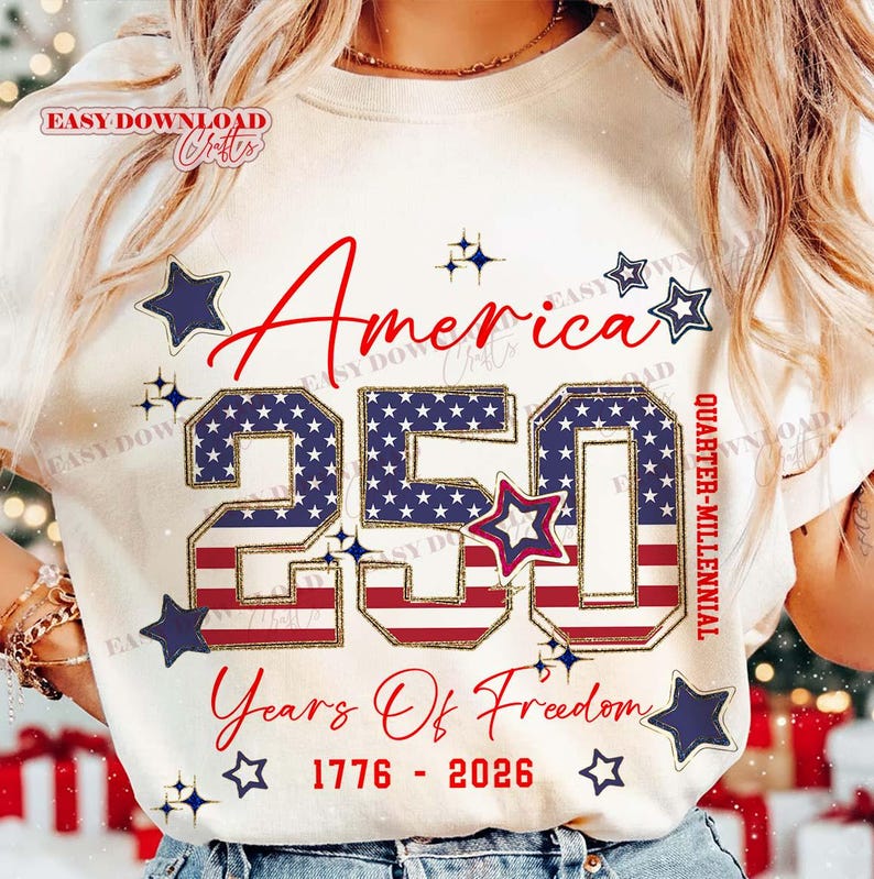 May include: Cream-colored t-shirt with the text "America 250 Years Of Freedom 1776-2026". The number 250 is filled with a blue star pattern and red stripes, surrounded by blue stars.