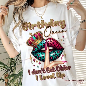 May include: White t-shirt with a graphic design featuring the text "Birthday Queen" in gold glitter lettering. The design includes a crown, lips with a teal and pink leopard print, and the text "I don't Get Older I Level Up".