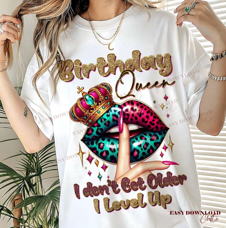 May include: White t-shirt with a graphic design featuring the text "Birthday Queen" in gold glitter lettering. The design includes a crown, lips with a teal and pink leopard print, and the text "I don't Get Older I Level Up".