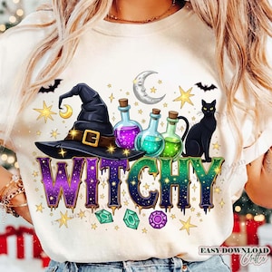 Puede incluir: Camiseta color crema con un diseño de bruja. El diseño incluye un sombrero de bruja negro con hebilla dorada, botellas de pociones, un gato negro y la palabra "WITCHY" en morado y verde. Estrellas, gemas y una luna creciente completan el tema de Halloween.