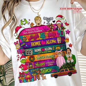 Puede incluir: Una camiseta blanca con una pila de car&aacute;tulas de cintas VHS coloridas con t&iacute;tulos de pel&iacute;culas navide&ntilde;as como Home Alone, Jingle All the Way, The Santa Clause, The Muppet Christmas Carol y How the Grinch Stole Christmas.