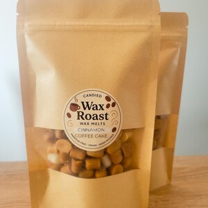 May include: Two brown paper bags of wax melts. The bags have a clear window showing the wax melts inside. The label reads "Wax Roast" with "Cinnamon Coffee Cake" and "Paraffin-Free Vegan Hand-Poured". The net weight is 4 oz.