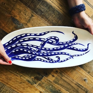 May include: White oval ceramic serving platter with a blue and white octopus design. The octopus tentacles are outlined in white and have white dots along the length of each tentacle.
