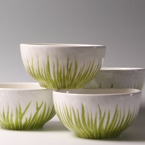May include: Four white ceramic bowls with a green grass design. The bowls are stacked on top of each other.