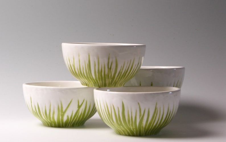 May include: Four white ceramic bowls with a green grass design. The bowls are stacked on top of each other.