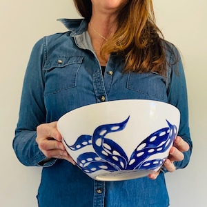 Pode incluir: Uma tigela grande de cerâmica branca com um design de polvo azul e branco. A tigela está sendo segurada por uma pessoa.