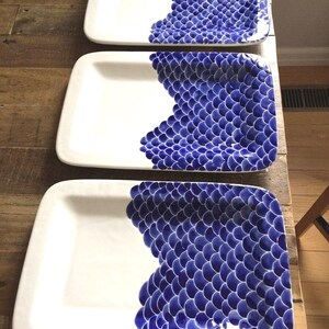 May include: Three white rectangular serving platters with a blue and white scale pattern on the right side of each platter.