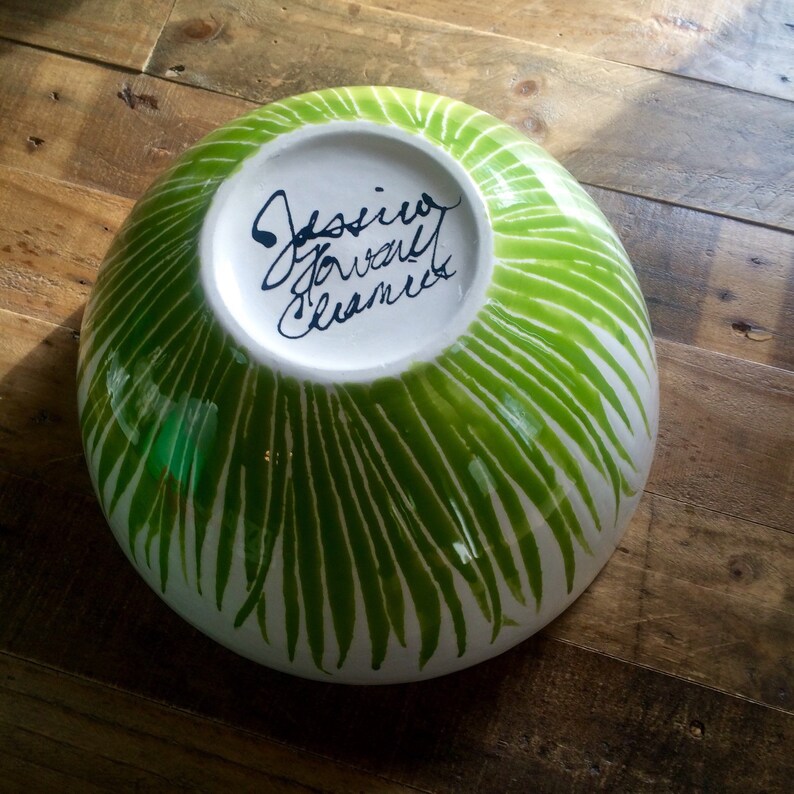 May include: A white ceramic bowl with a green and white striped pattern. The bowl is signed "Jessie  Gowell Ceramics" on the bottom.