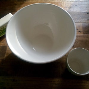 May include: A white ceramic mixing bowl and a smaller white ceramic cup on a wooden surface.