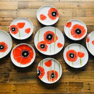 May include: Set of ten white ceramic dinner plates with hand-painted red poppy flower designs. The plates have a white background with green stems and leaves.