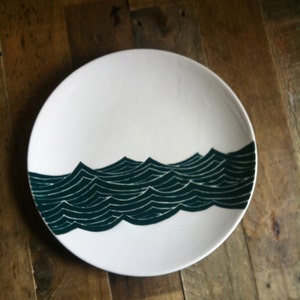 May include: White ceramic plate with a dark green wave design. The waves are stylized and create a repeating pattern.