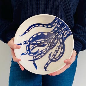 May include: A white ceramic bowl featuring a blue and white octopus design. The octopus tentacles are curled and have white dots on them.