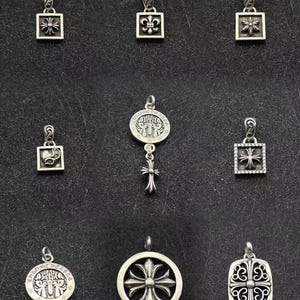 May include: A collection of silver pendants with various designs, including crosses, fleur-de-lis, and other ornate patterns. The pendants are displayed against a dark background, showcasing their intricate details and craftsmanship.