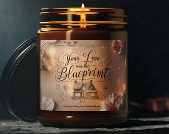 May include: A brown glass candle jar with a gold lid. The label on the jar says "Your Love was the Blueprint" with a drawing of a house and flowers. The text "Every good thing I am started with you" is also on the label.