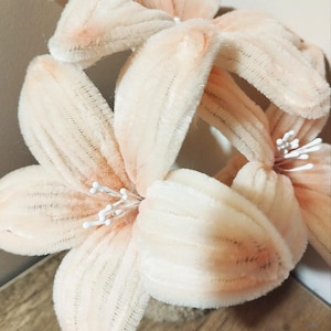 May include: Close-up of a cluster of soft, peach-coloured artificial flowers. The petals have a textured, velvety appearance with subtle shading. White, spiky stamens emerge from the centre of each bloom. The flowers are arranged in a decorative display.