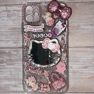 May include: Clear phone case decorated with pink glitter, Hello Kitty mirror, and various charms. Charms include a pink bow, a Hello Kitty boba drink, and a pink purse. Text on the case reads "I'M LITERALLY JUST A GIRL" and "GRL PWR".