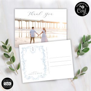 Op de afbeelding: Een trouwbedankkaart met een strandfoto en een stel dat elkaars hand vasthoudt. De voorkant zegt "Thank You" in sierlijke letters. De achterkant heeft een bloemenontwerp met de initialen "A M" en de namen "Ashley & Mitch".