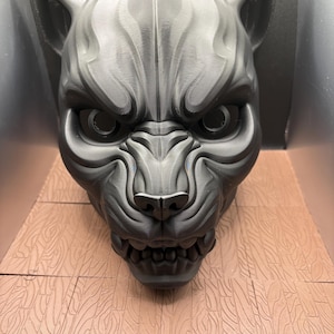 Puede incluir: Una escultura gris impresa en 3D de una feroz cabeza de felino. La escultura presenta texturas de pelaje detalladas, dientes afilados y ojos intensos. La cabeza de gato es una llamativa obra de arte.