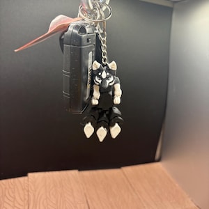 May include: A black and white keychain charm in the shape of a stylized animal, hanging with keys and a car remote. The charm has white paws and a white face with black markings. The keychain is attached to a silver carabiner.