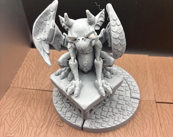 Può includere: Statuetta di gargoyle grigio con ali dettagliate, corna e piedi artigliati. La statua è appollaiata su una base quadrata sopra una piattaforma circolare con un motivo a ciottoli. L'oggetto è un elemento decorativo a tema fantasy.
