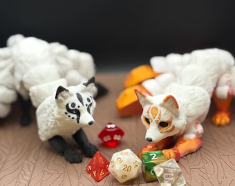 May include: Two white fox figurines with multiple tails, black paws, and detailed facial markings. The foxes are surrounded by various polyhedral dice in red, white, green, and clear colors. The background is a dark brown.