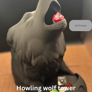 May include: A 3D-printed, dark grey howling wolf dice tower. The wolf's mouth holds a red die with white numbers. The base of the tower contains several dice. The text "Howling wolf tower" is visible.