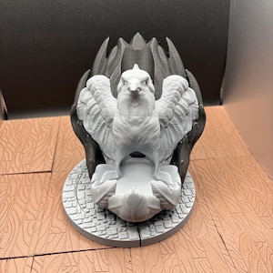 May include: A 3D-printed sculpture of a bird with outstretched wings, in shades of gray and black. The bird is perched on a circular base with a detailed pattern. The sculpture has a detailed feather design and is set against a dark background.