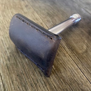 May include: A silver safety razor with a brown leather case. The razor has a textured handle and a chrome finish.