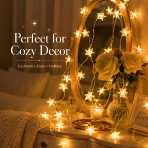 May include: A string of warm white star-shaped fairy lights draped over a vanity. The lights are illuminating a bedroom scene with a mirror, flowers, and a candle. Text reads "Perfect for Cozy Decor".