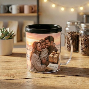 Puede incluir: Una taza de vidrio transparente con borde negro muestra un retrato familiar contra un fondo de puesta de sol. La taza tiene un asa y una pequeña caja de regalo con un lazo. Las palabras "Thank You" están impresas en una tarjeta pequeña.