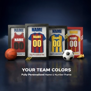 May include: Four framed sports jerseys with the word "NAME" above and the number "00" below. A basketball, soccer ball, and gold cleats are in front. The text "YOUR TEAM COLORS" and "Fully Personalized Name & Number Frame" are at the bottom.