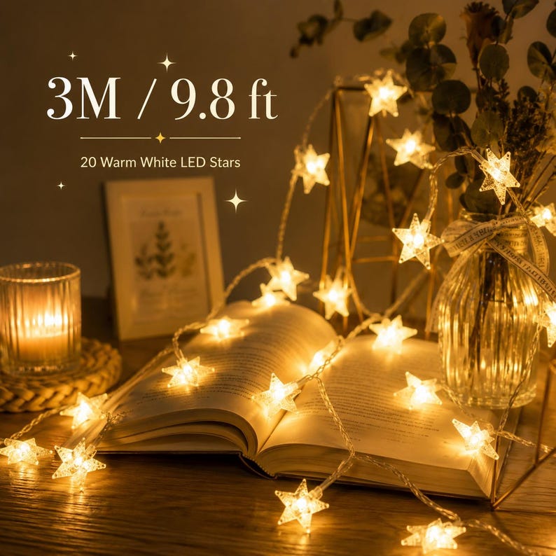 May include: A string of 20 warm white LED star lights, 9.8 ft long, draped over an open book. The lights are illuminated, casting a warm glow. The image also includes a candle, a framed picture, and a vase with greenery.