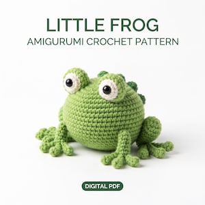 May include: A green amigurumi crochet frog with large white eyes and black pupils. The text above reads LITTLE FROG AMIGURUMI CROCHET PATTERN, and the text below reads DIGITAL PDF. The frog has a round body, textured skin, and webbed feet.
