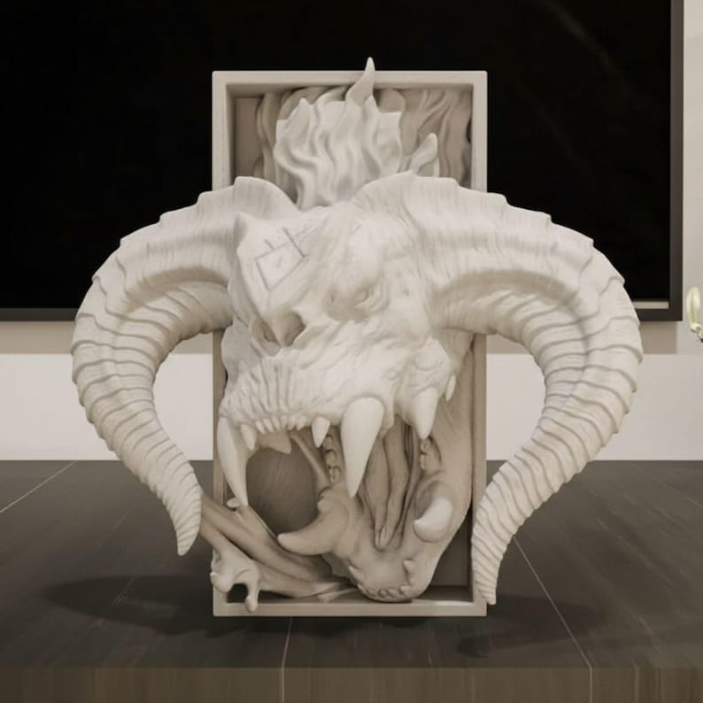 May include: A white, detailed sculpture of a horned demon skull with large teeth and a fiery mane. The sculpture is set within a rectangular frame, showcasing the intricate design and texture of the mythical creature.