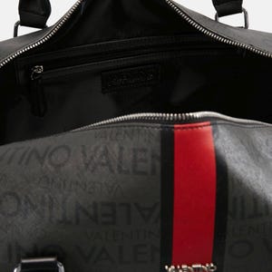 May include: Black duffel bag with the Valentino logo and text pattern. The bag features a red stripe down the center, black handles, and a zippered main compartment. The interior is black.