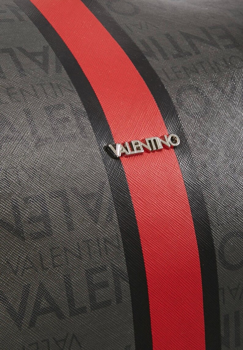 May include: Close-up of a textured gray fabric with a red stripe and a black stripe. The word "VALENTINO" is printed repeatedly on the gray fabric. A silver "VALENTINO" logo is centered on the red stripe.