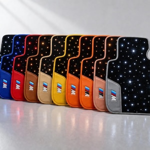May include: A collection of car floor mats in various colors, each featuring a black base with illuminated star-like lights. The mats have colored borders and the "M" logo. The mats are designed to fit a car.