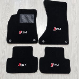 Op de afbeelding: Een set van vier zwarte automatten met het rood-witte RS4-logo geborduurd op elk stuk. De bestuurdersmat bevat een getextureerd hielstuk en twee ronde bevestigingsringen, terwijl de andere matten ook zijn voorzien van bijpassende ringen.