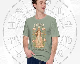 May include: Sage green t-shirt featuring a Libra zodiac design. The graphic includes the word "LIBRA" above an illustration of a woman holding scales, surrounded by lotus flowers. The text "PURE AND JUST" is below the illustration. A zodiac wheel is in the background.
